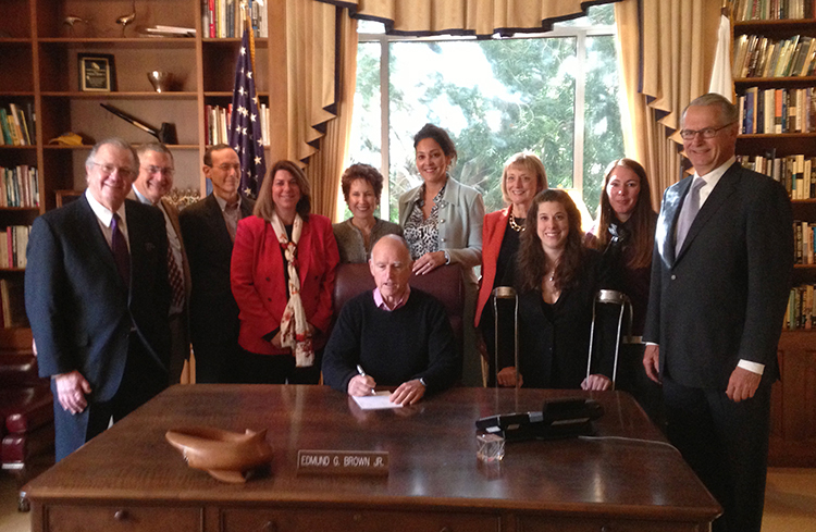 The authors and sponsors of the Self Determination Bill stand around Governor Jerry Brown while he signs the bill at his desk, all smiling