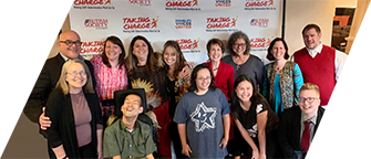 At the 2019 Self Determination Conference, the DVU board stands in two lines in front of a white backdrop with the DVU and conference logos, all smiling