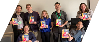 A group of DVU board members and staff pose with their book, Profiles in Self Determination. One man in a wheelchair holds the book with his toes.