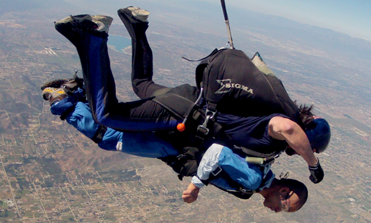 An Asian man with a disability skydiving, strapped to an instructor
